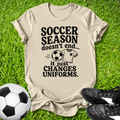 Beige t-shirt with soccer-themed text on grass with soccer ball and shoes