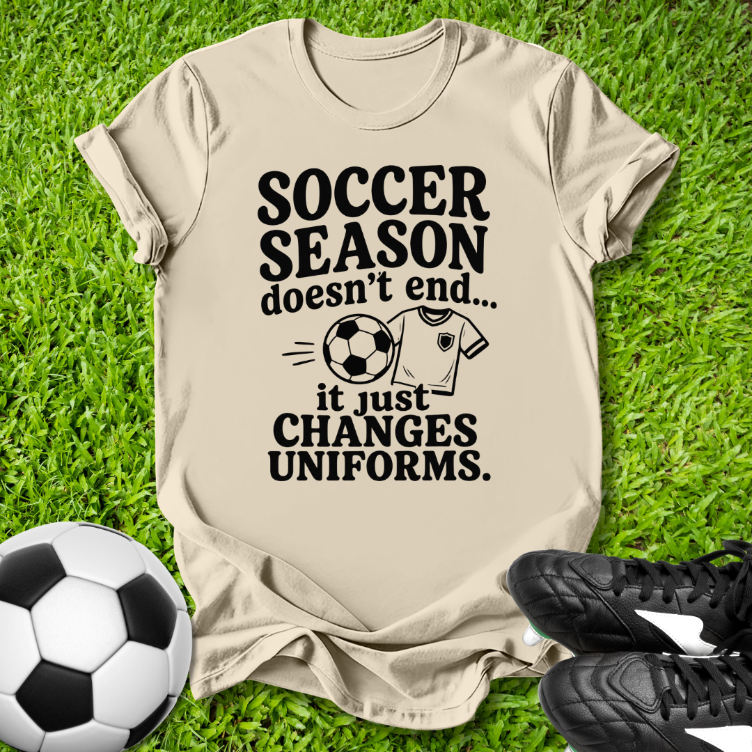 Beige t-shirt with soccer-themed text on grass with soccer ball and shoes