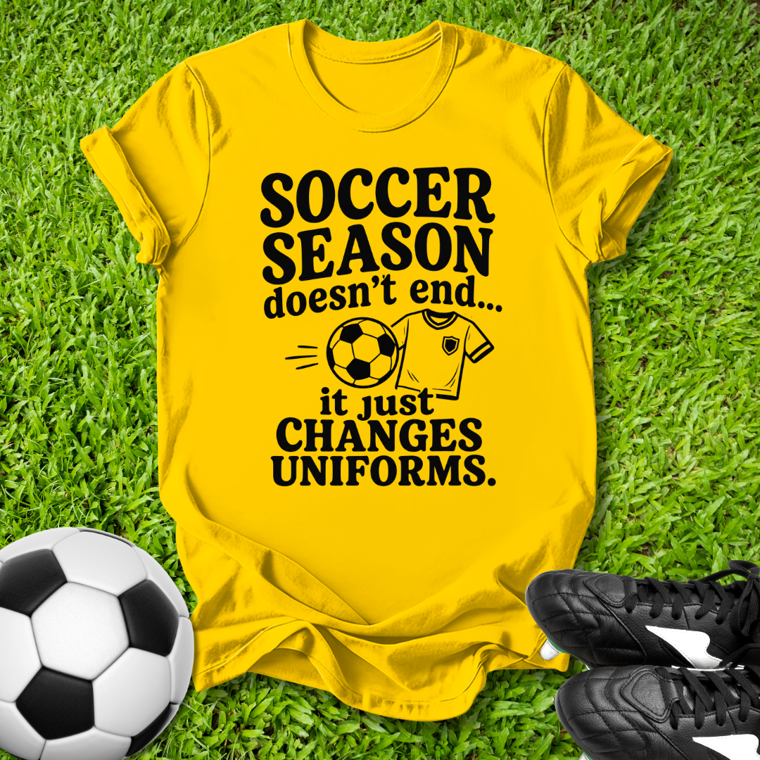 Yellow t-shirt with 'Soccer Season doesn't end...' text on grass with soccer ball and shoes.
