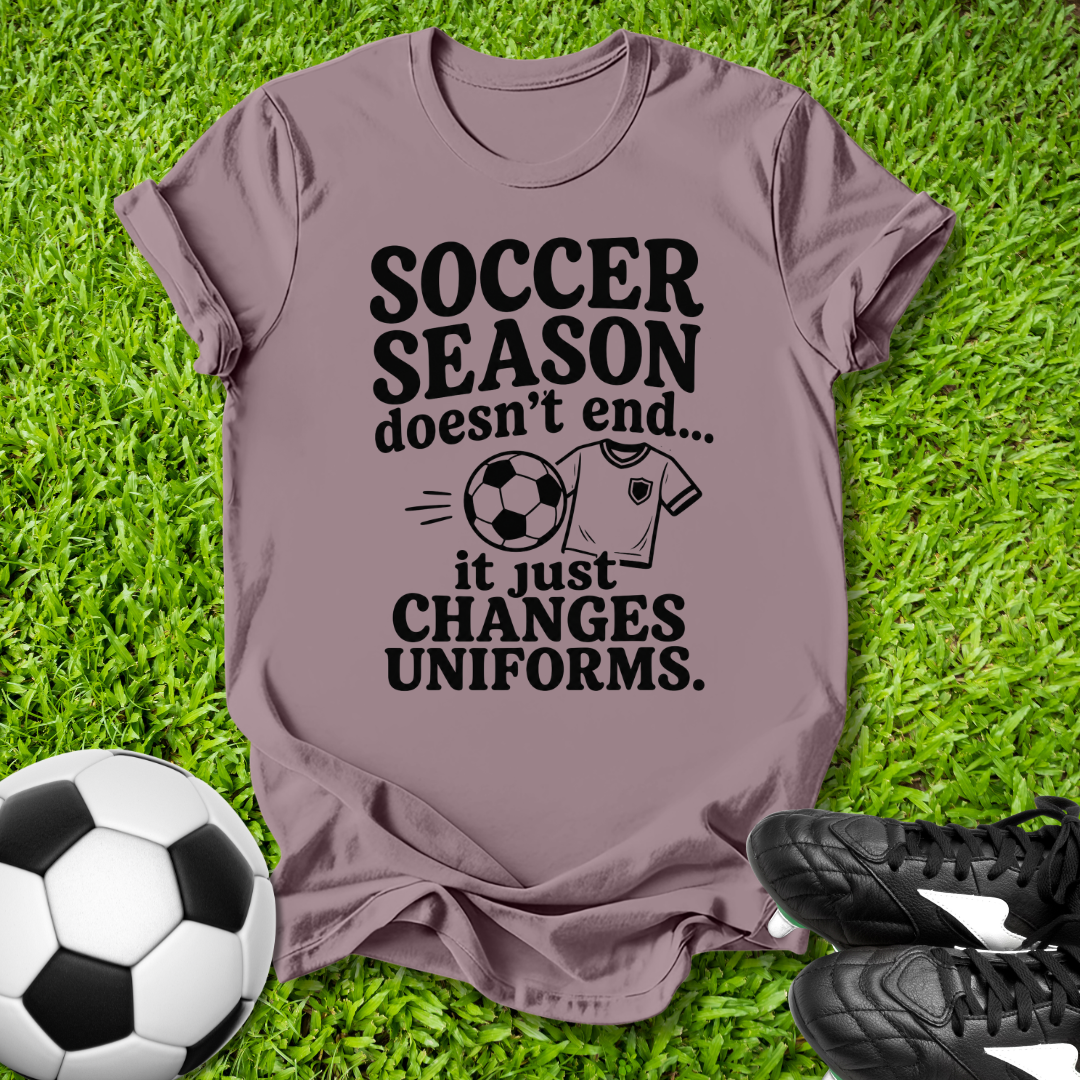 Purple t-shirt with 'Soccer Season doesn't end...' text on grass with soccer ball and shoes.