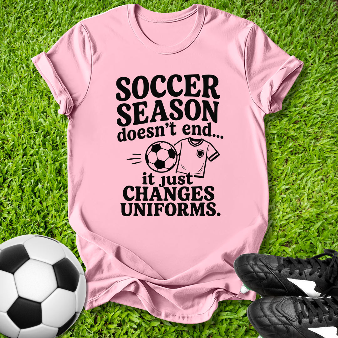 Pink t-shirt with 'Soccer Season doesn't end...' text on grass with soccer ball and shoes.