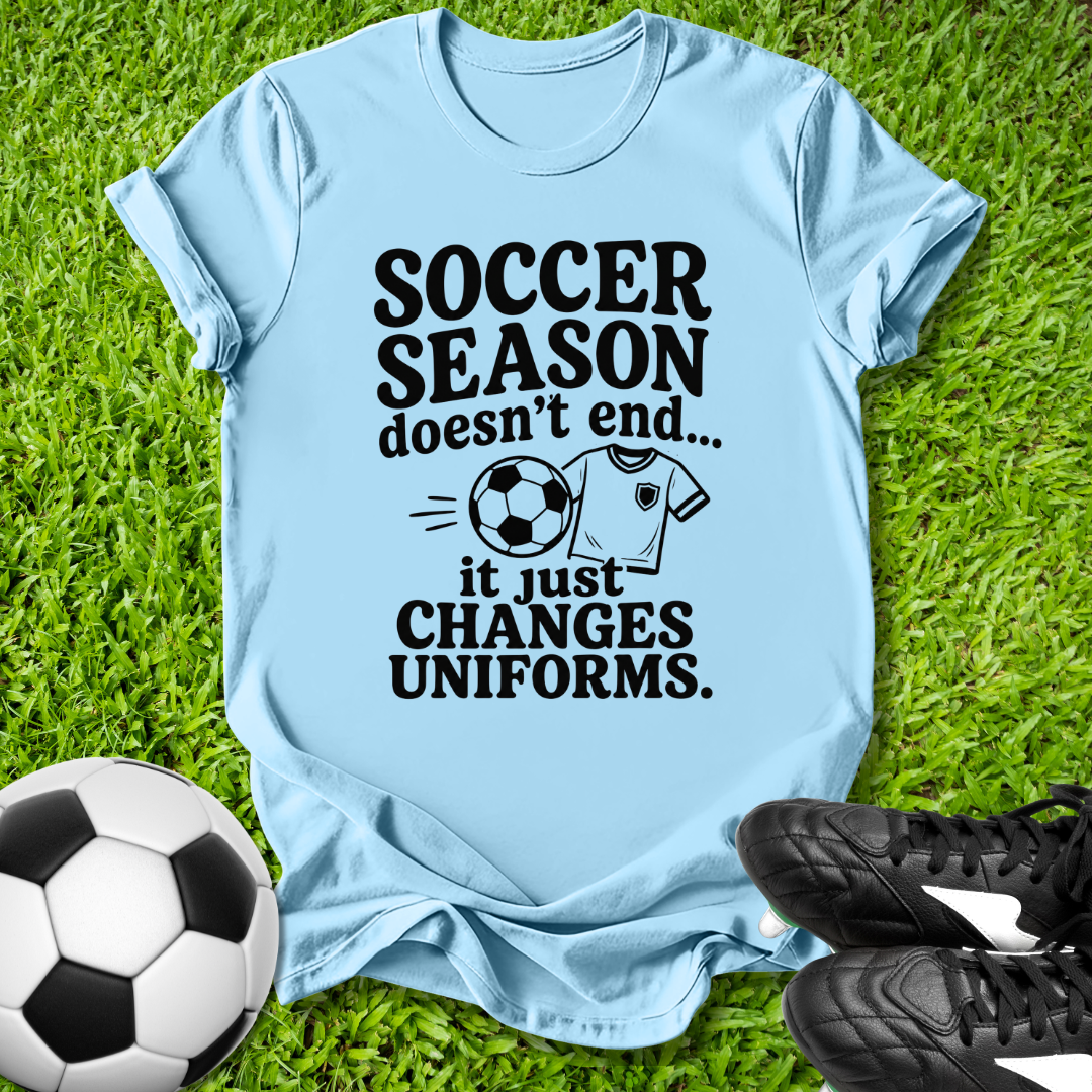 Light t-shirt with 'Soccer Season doesn't end...' text on grass with soccer ball and shoes.