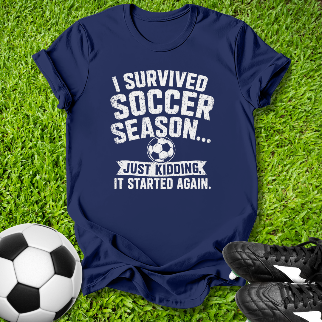 Navy blue t-shirt with humorous soccer text on grass with soccer ball and shoes
