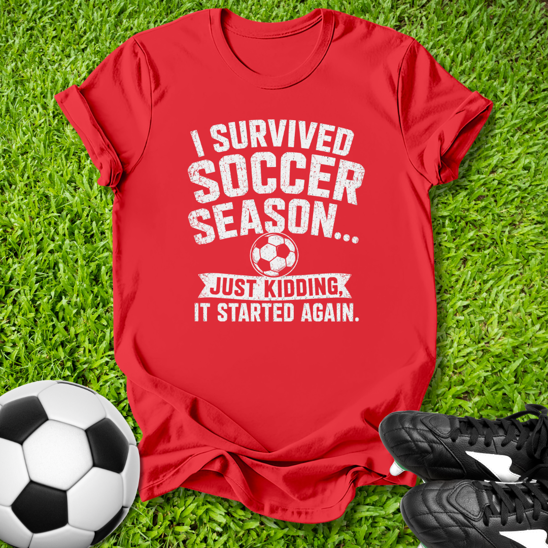 Red t-shirt with humorous soccer text on grass with soccer ball and shoes