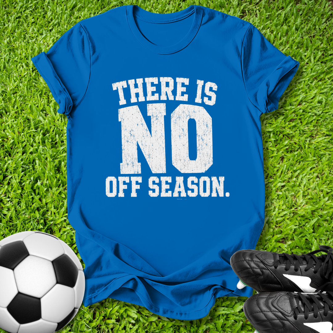 Blue t-shirt with 'There is no off season' text on grass with soccer ball and shoes.