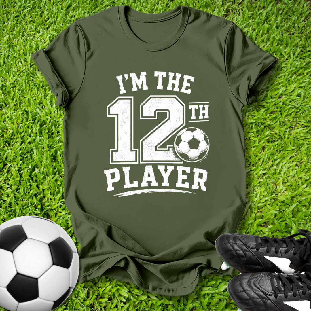 Green t-shirt with 'I'm the 12th Player' text on grass with soccer ball and shoes.