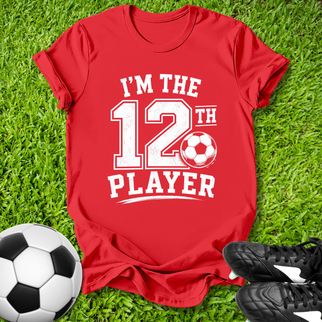 Red t-shirt with 'I'm the 12th Player' text on grass with soccer ball and shoes.