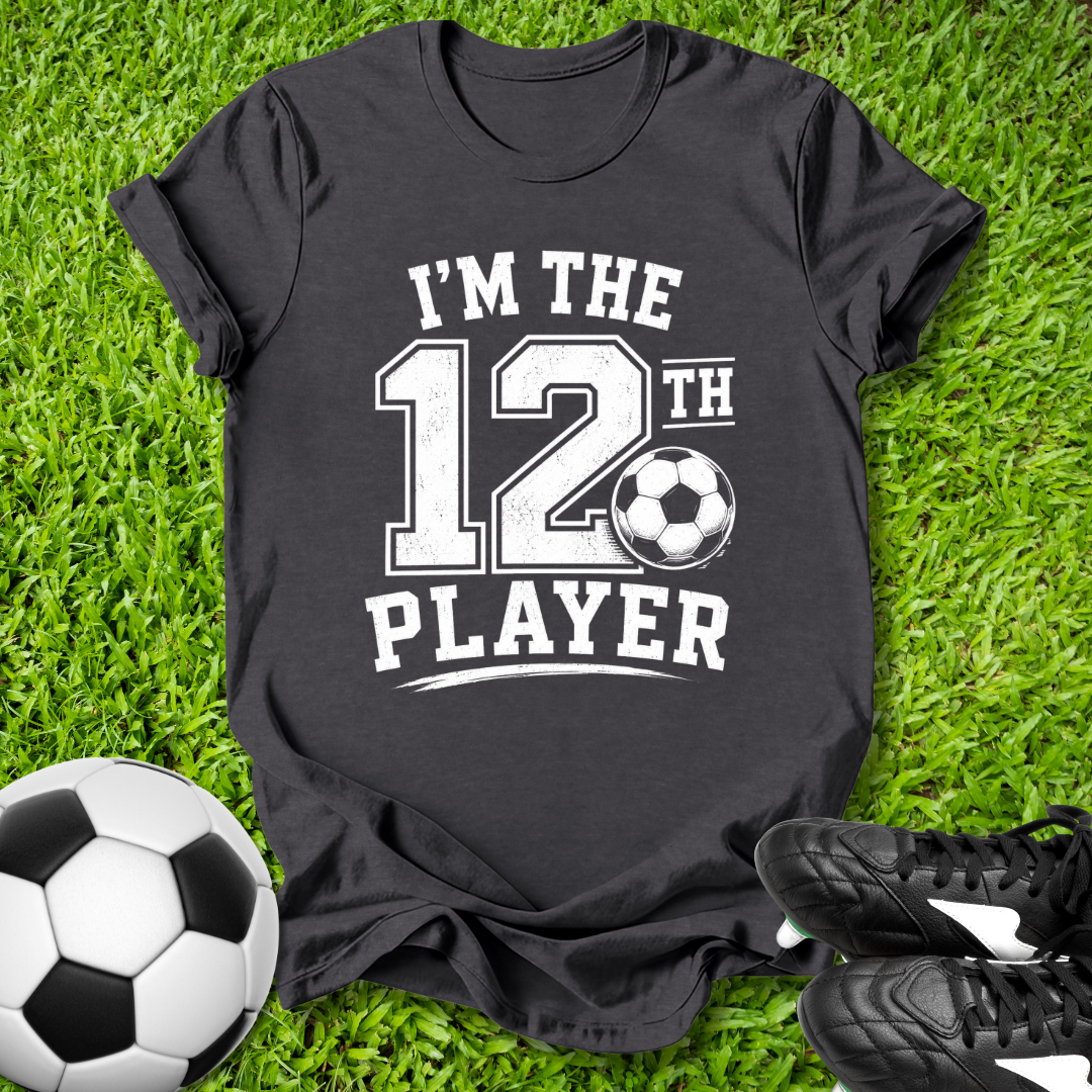 Black t-shirt with 'I'm the 12th Player' text on grass with soccer ball and shoes.
