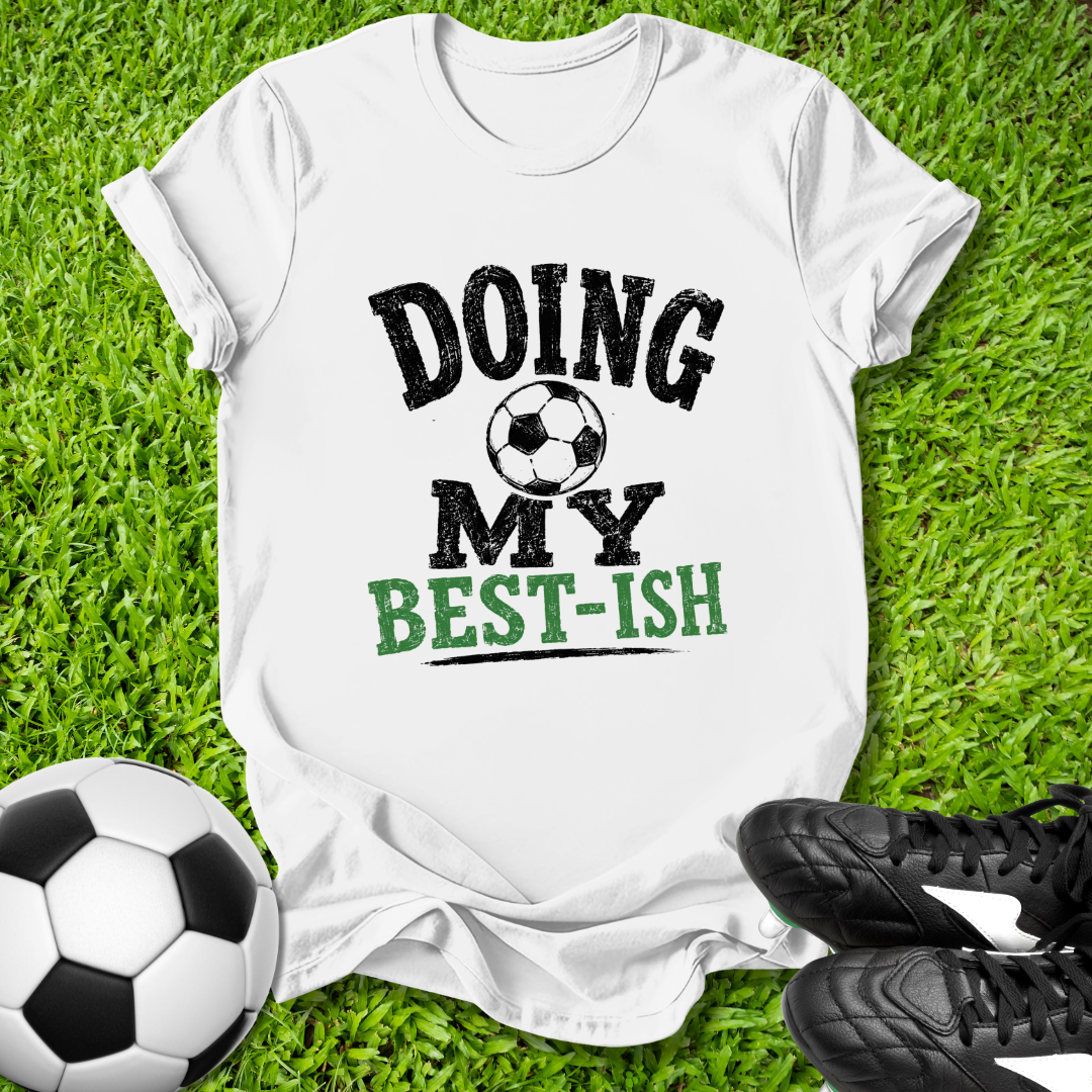White t-shirt with 'Doing My Best-ish' text on grass with soccer ball and shoes