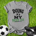 Gray t-shirt with 'Doing My Best-ish' text on grass with soccer ball and shoes