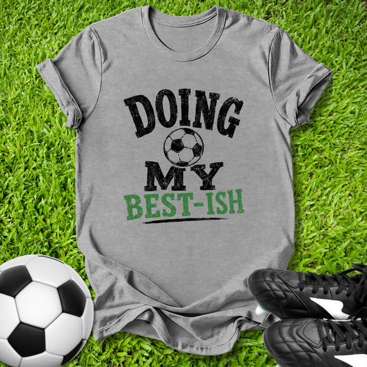 Gray t-shirt with 'Doing My Best-ish' text on grass with soccer ball and shoes