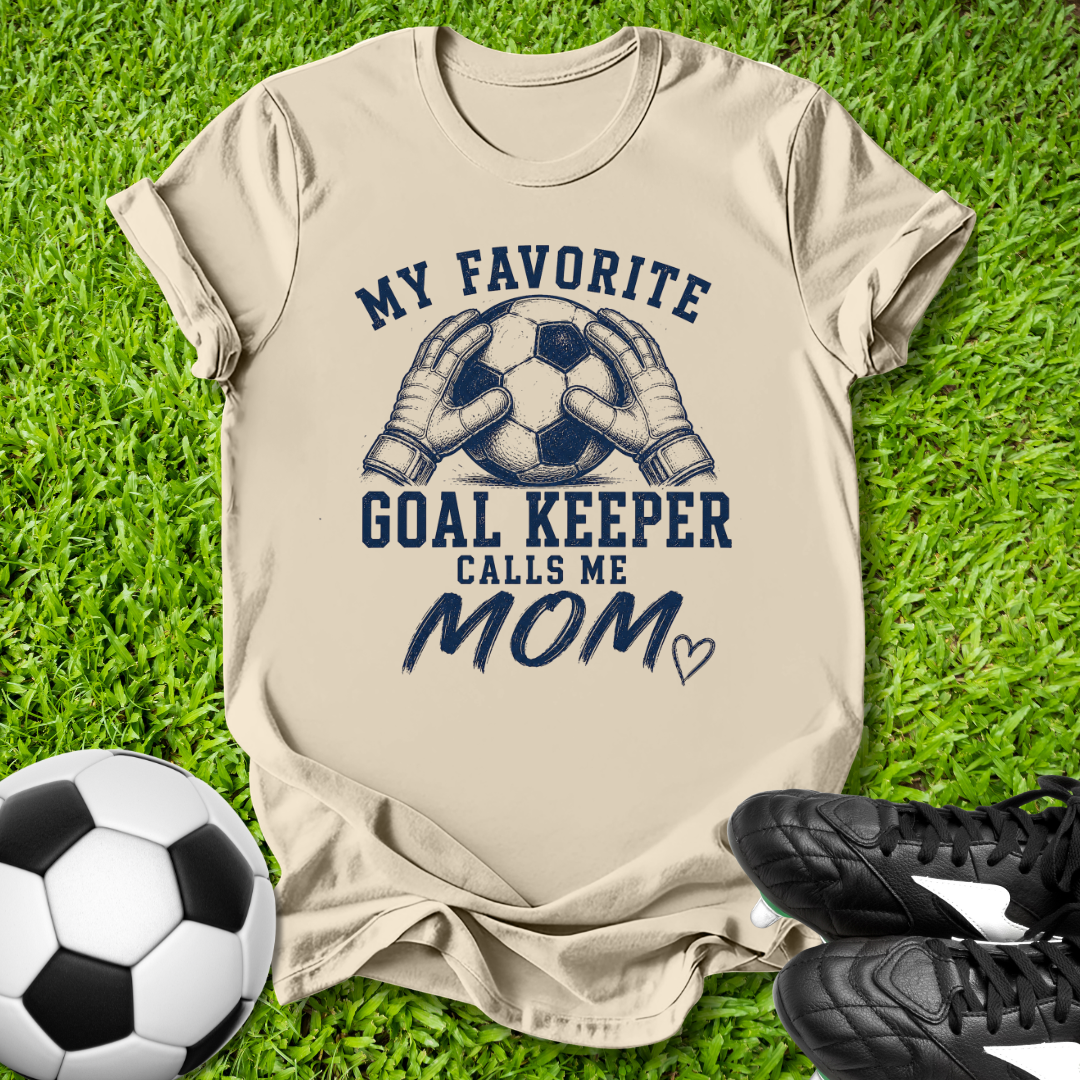 Beige t-shirt with soccer-themed design on grass with soccer ball and shoes