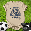 Beige t-shirt with soccer-themed text on grass with soccer ball and shoes
