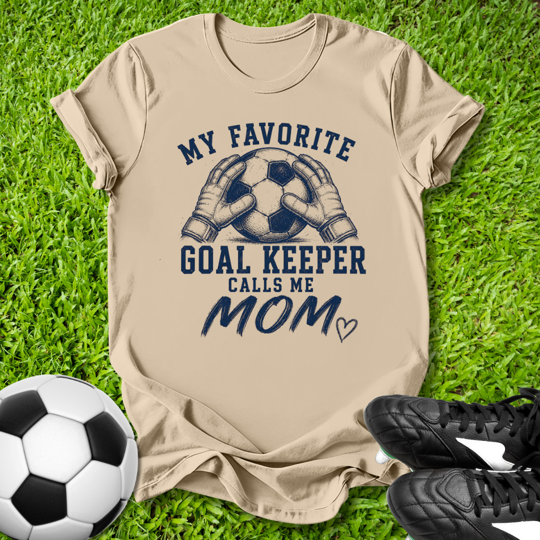 Beige t-shirt with soccer-themed text on grass with soccer ball and shoes