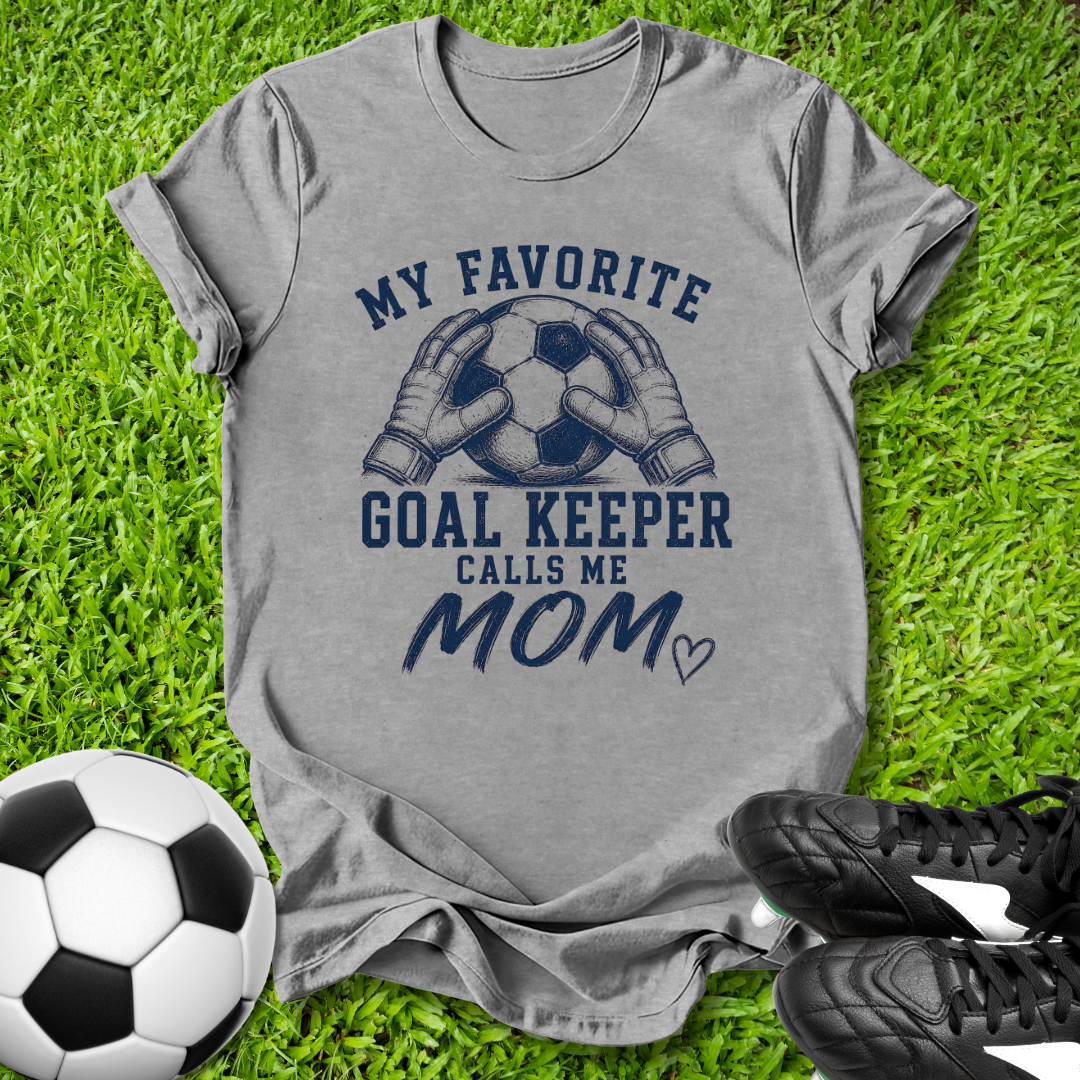 Gray t-shirt with 'My Favorite Goal Keeper Calls Me Mom' text on grass with soccer ball and shoes.