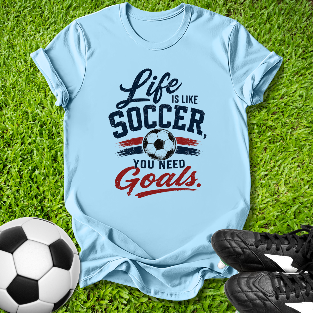 Light blue t-shirt with soccer-themed text on grass with a soccer ball and shoes.