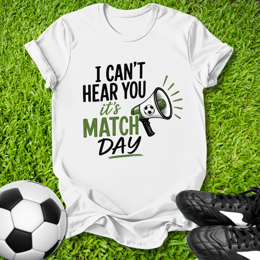 White t-shirt with 'I can't hear you, it's match day' text on grass with soccer ball and cleats.