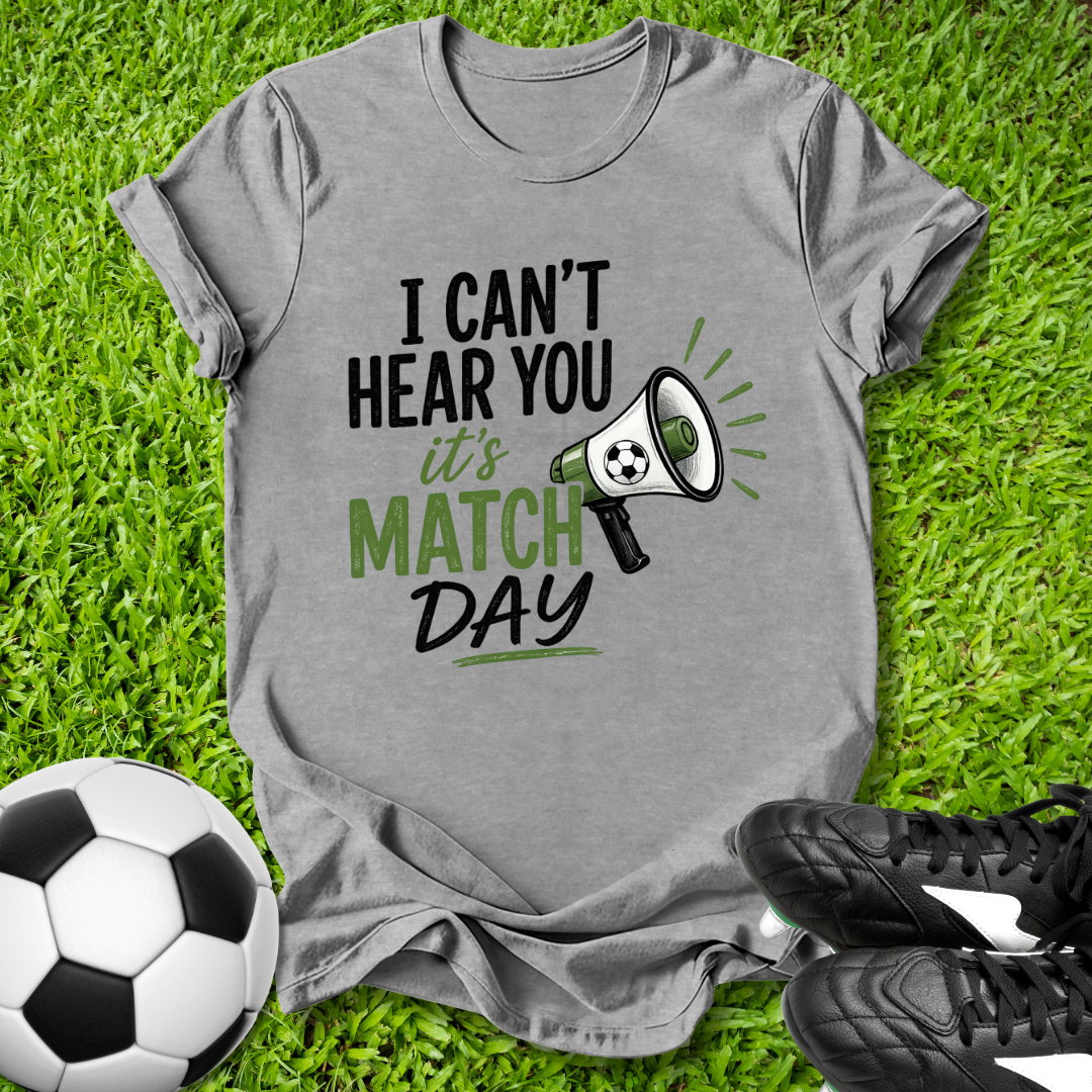 Gray t-shirt with 'I can't hear you, it's match day' text on grass with soccer ball and shoes.