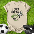Beige t-shirt with 'I can't hear you, it's match day' text on grass with soccer ball and shoes.