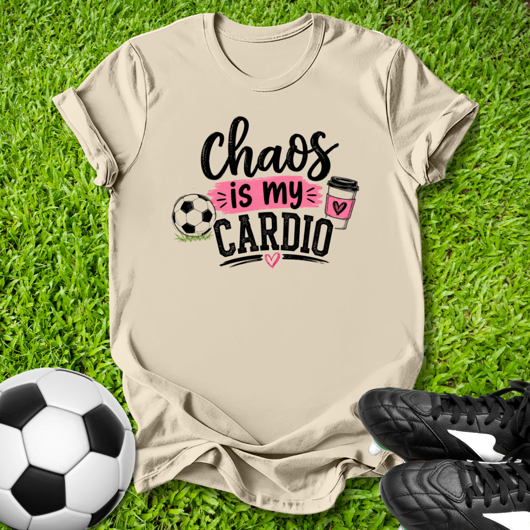 Beige t-shirt with 'Chaos is my Cardio' text on grass with soccer ball and shoes.