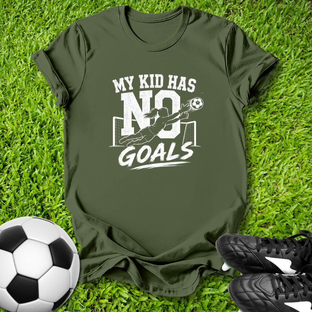 Green t-shirt with 'My kid has no goals' print on grass with soccer ball and shoes.