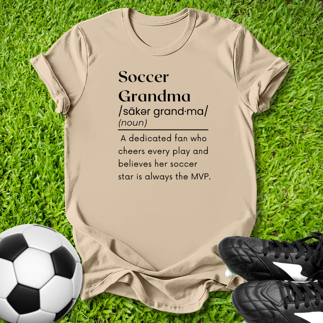 Beige t-shirt with 'Soccer Grandma' definition on grass with soccer ball and shoes.