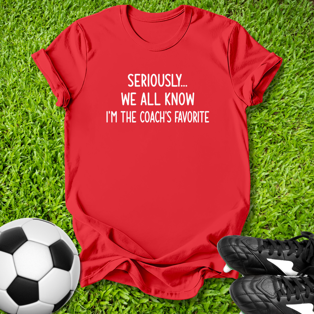 Red t-shirt with humorous text on grass with soccer ball and shoes