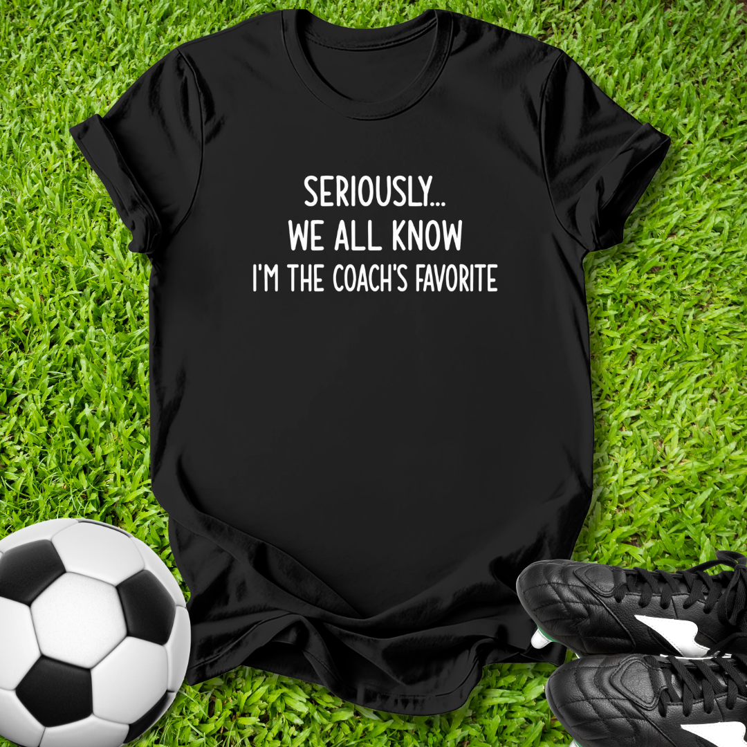 Black t-shirt with humorous text on grass with soccer ball and shoes