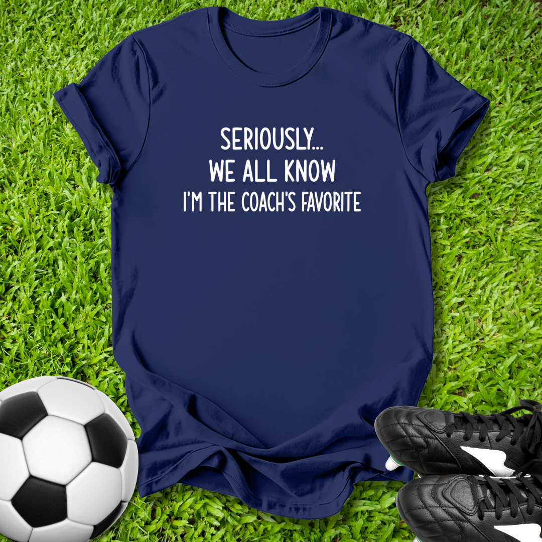 Navy blue t-shirt with humorous text on grass with soccer ball and shoes
