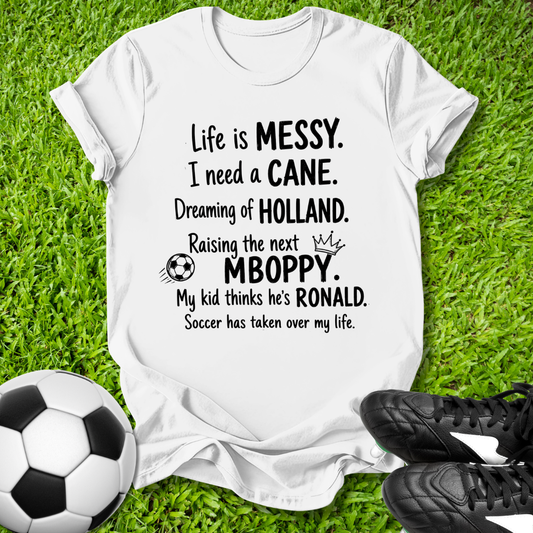 White t-shirt with humorous text on grass with soccer ball and shoes