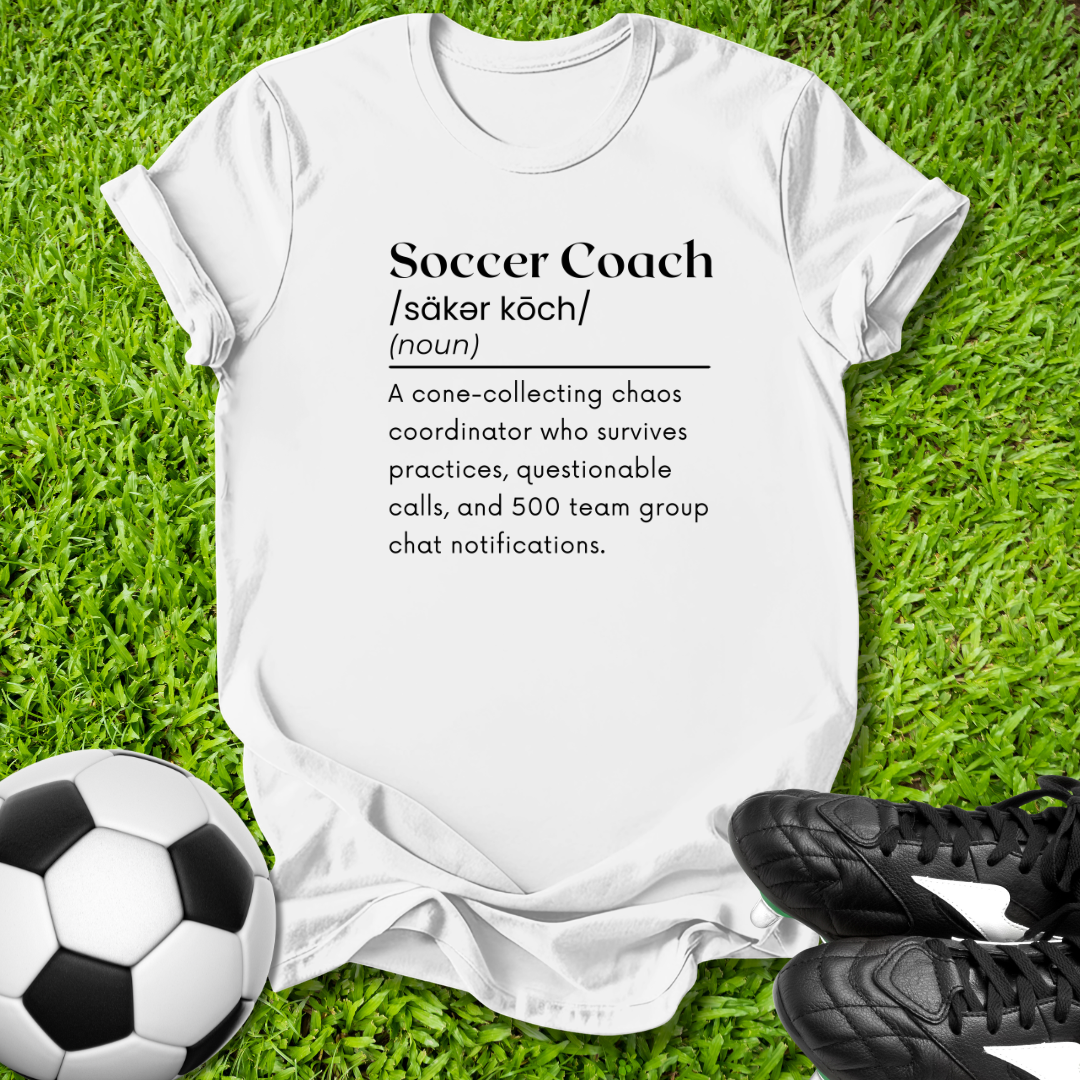 White t-shirt with soccer coach definition on grass with soccer ball and shoes