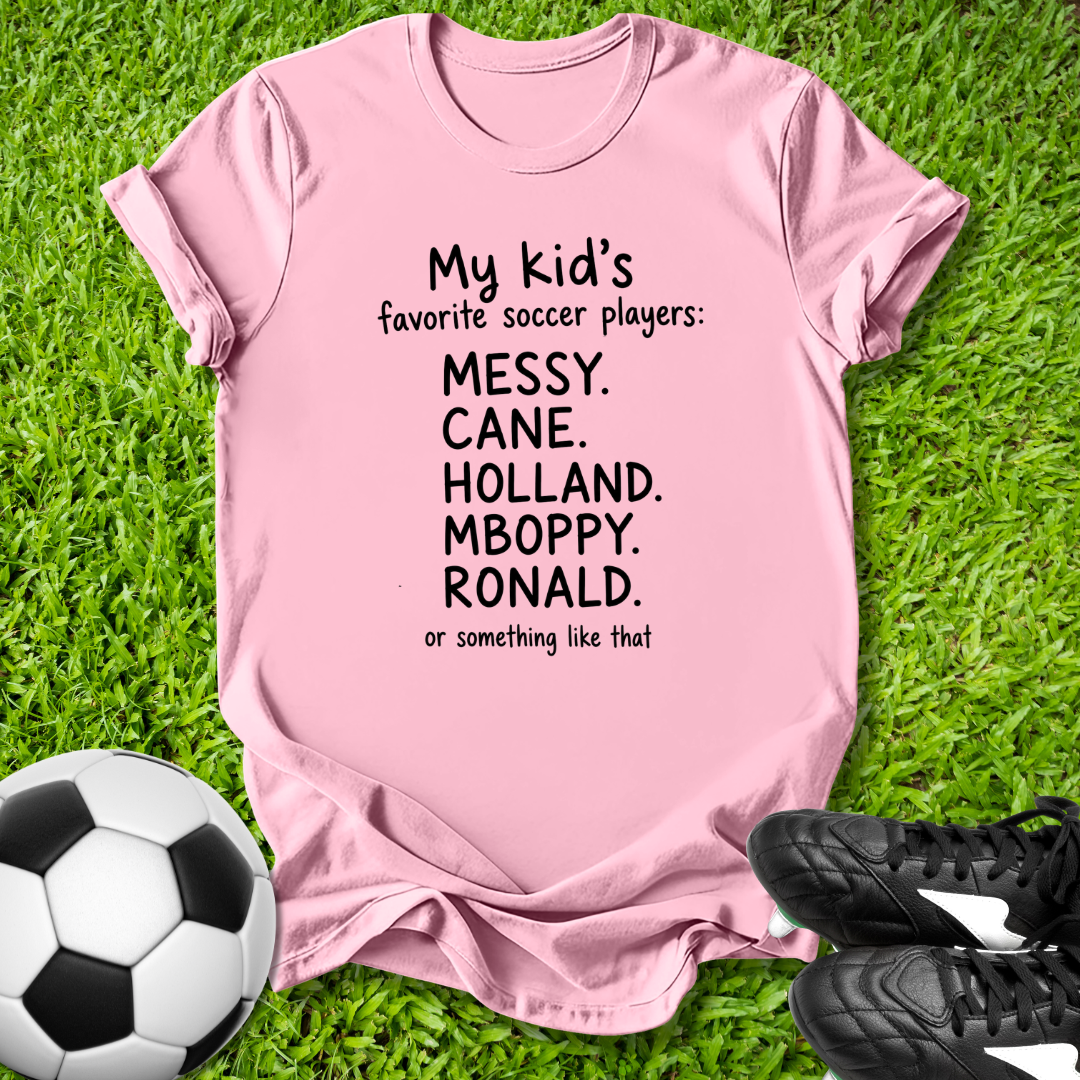 Pink t-shirt with humorous text on grass with soccer ball and shoes