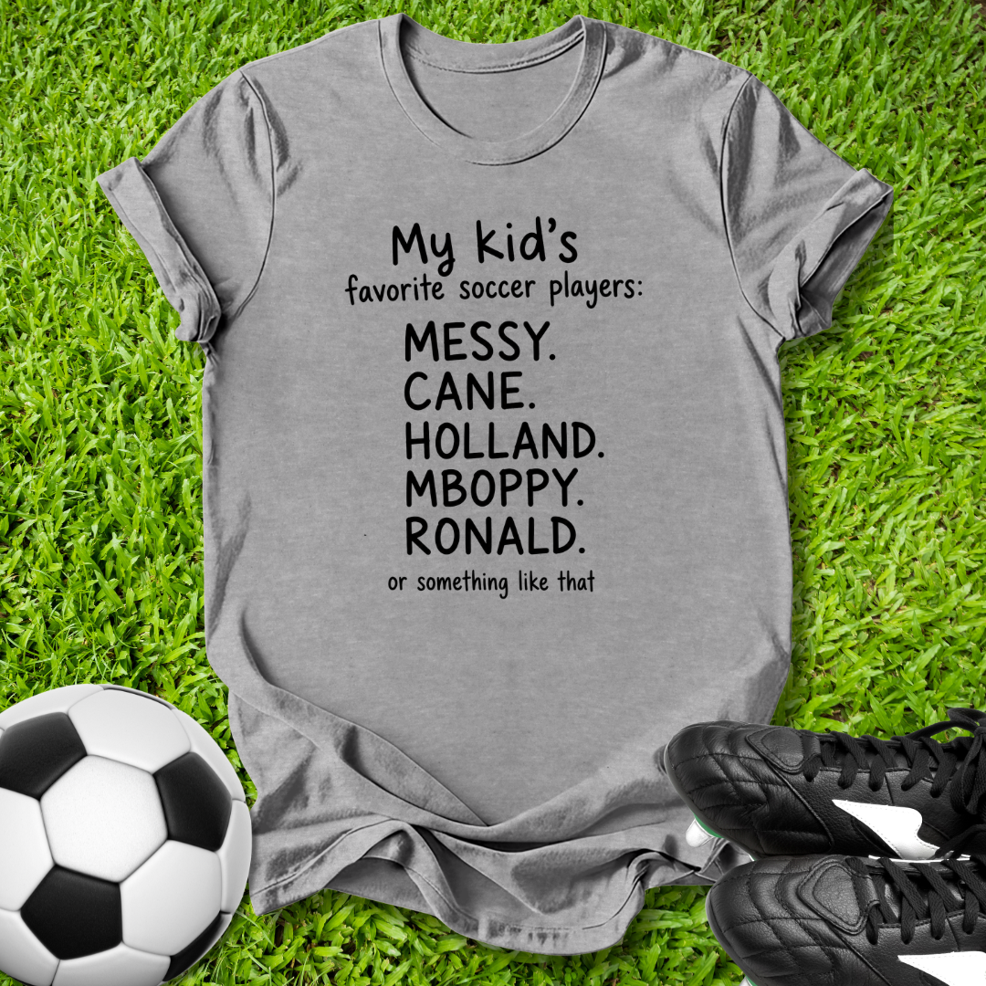 Gray t-shirt with humorous soccer player names on grass with soccer ball and shoes