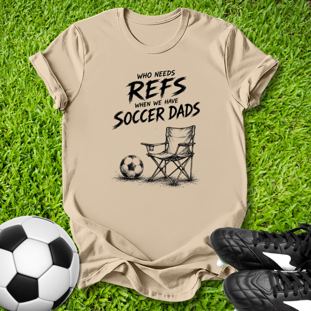 Beige t-shirt with soccer-themed text on grass with soccer ball and shoes.