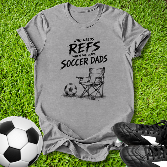 Gray t-shirt with soccer-themed text and graphics on grass with soccer ball and shoes.