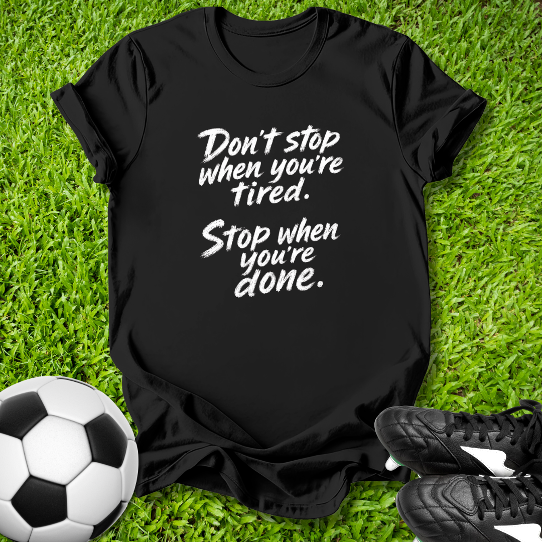Black t-shirt with motivational quote on grass with soccer ball and shoes