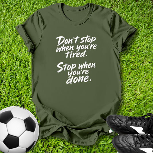 Green t-shirt with motivational quote on grass with soccer ball and shoes