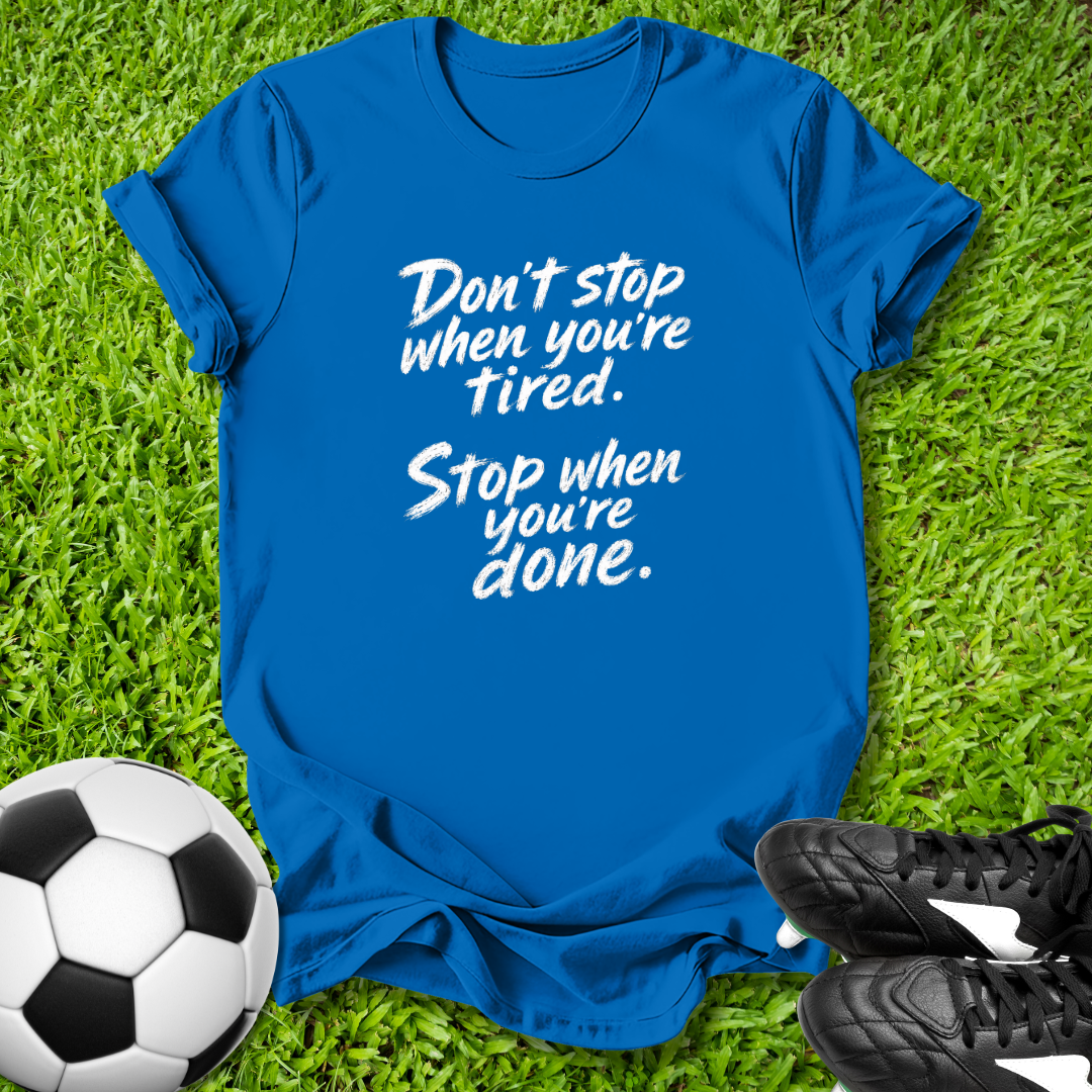 Blue t-shirt with motivational quote on grass with soccer ball and shoes