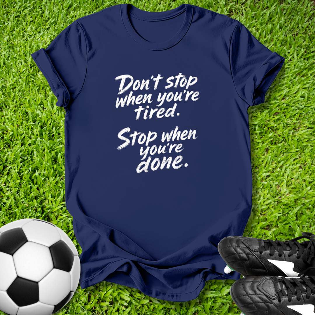 Navy blue t-shirt with motivational quote on grass with soccer ball and shoes