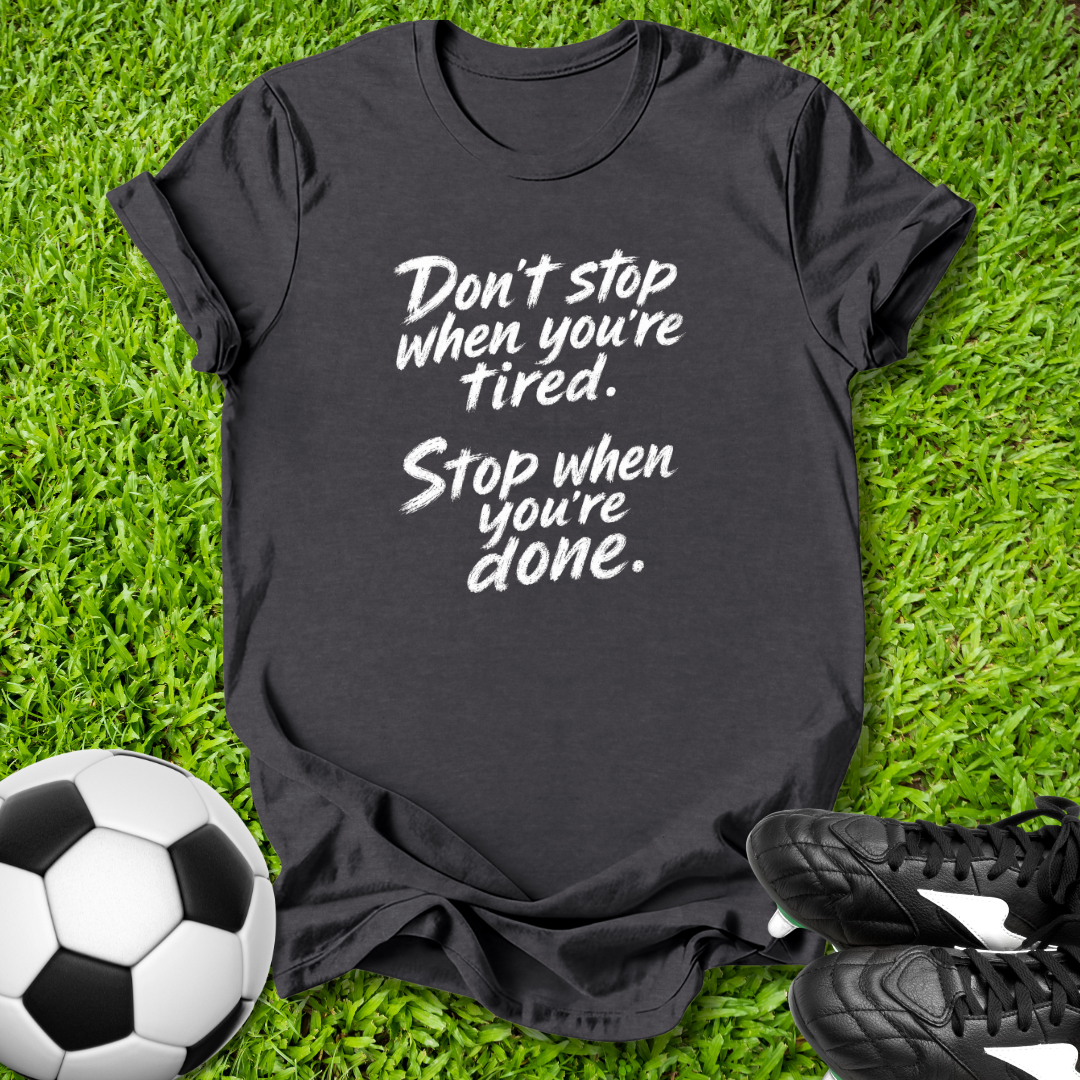 Black t-shirt with motivational quote on grass with soccer ball and shoes