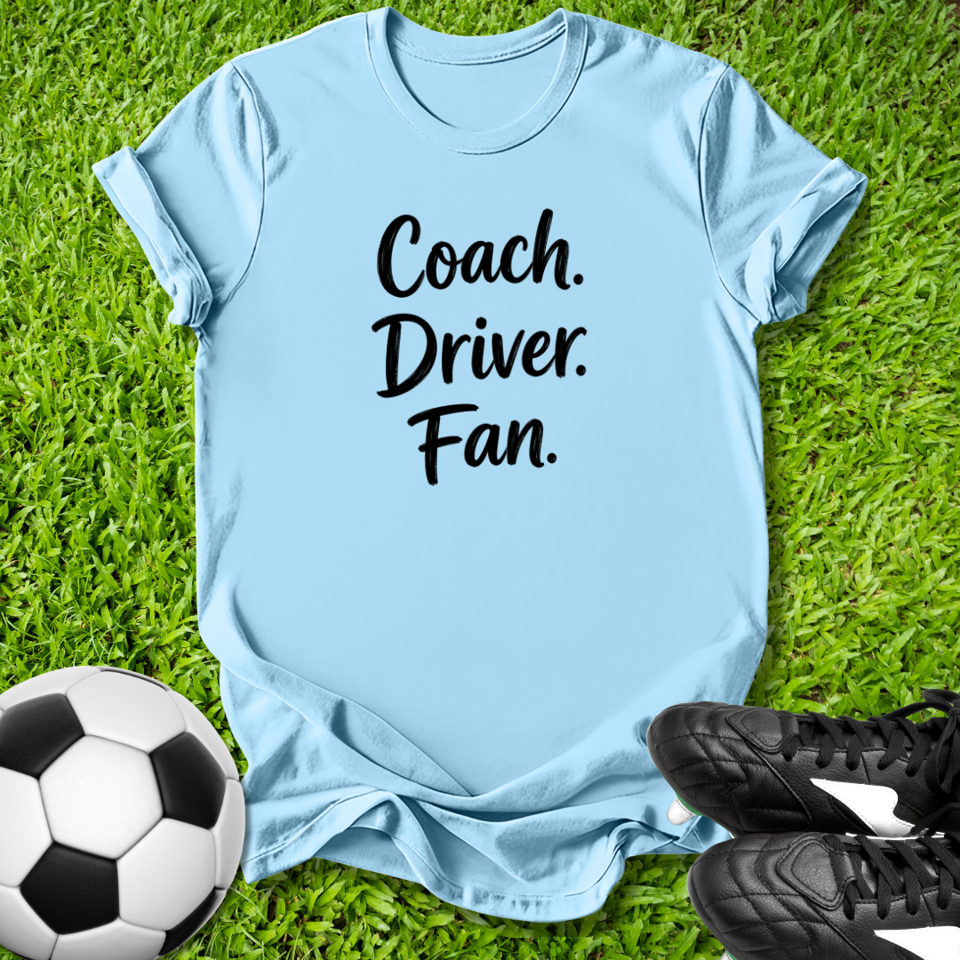 Light blue t-shirt with 'Coach. Driver. Fan.' text on grass with soccer ball and shoes.