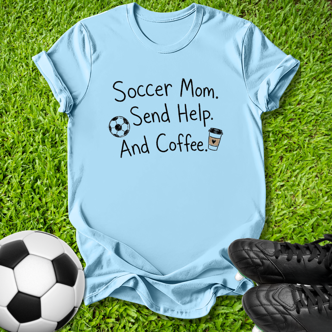 A light blue graphic t-shirt laid flat on green grass, featuring the text 'Soccer Mom. Send Help.