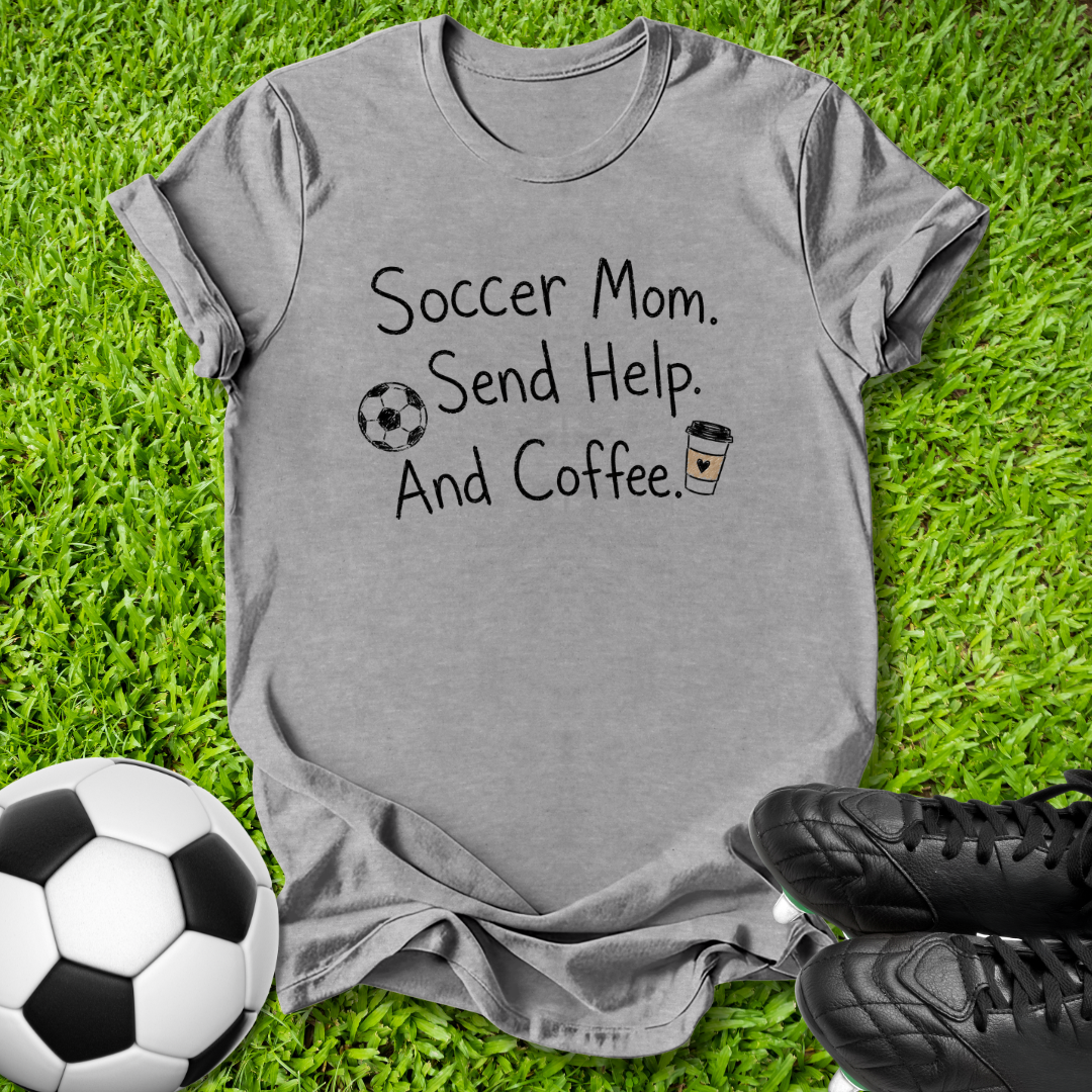 A heather gray graphic t-shirt laid flat on green grass, featuring the text 'Soccer Mom. Send Help.