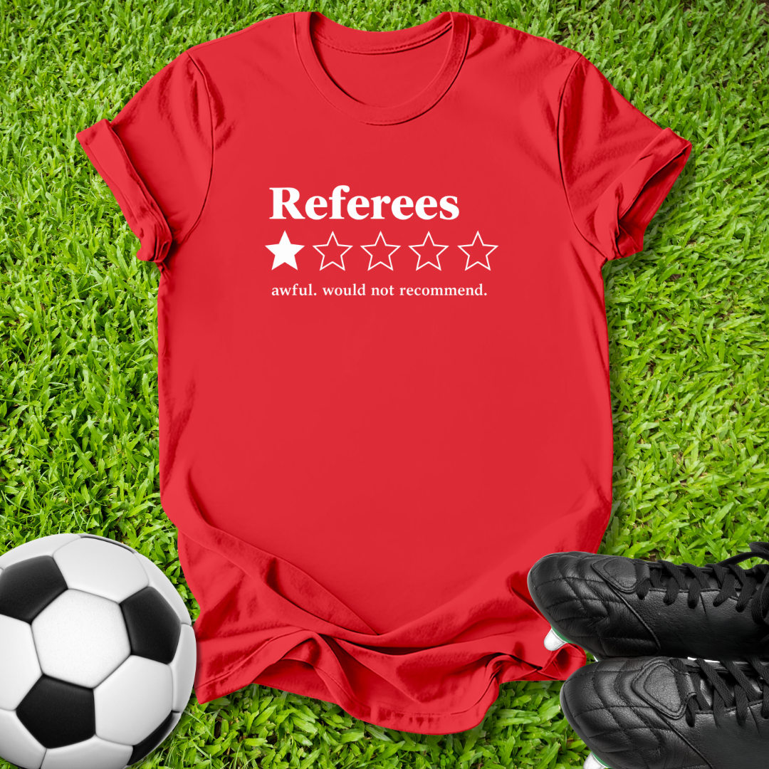 A red short-sleeve t-shirt with a white graphic reading 'Referees' and a one-star rating, styled on green grass with a soccer ball and black cleats.