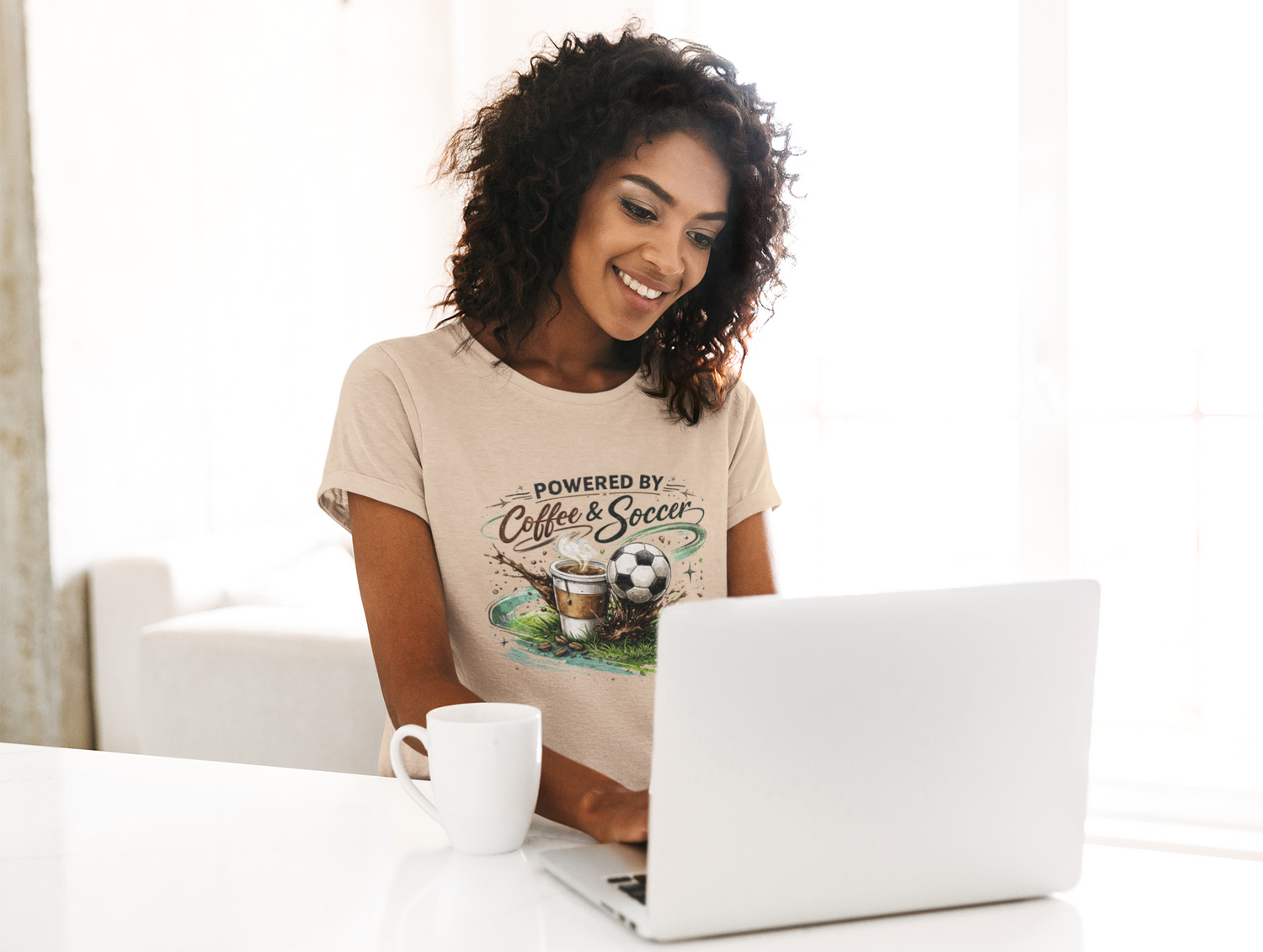 Woman wearing a t-shirt with 'Powered by Coffee & Soccer' design, using a laptop.
