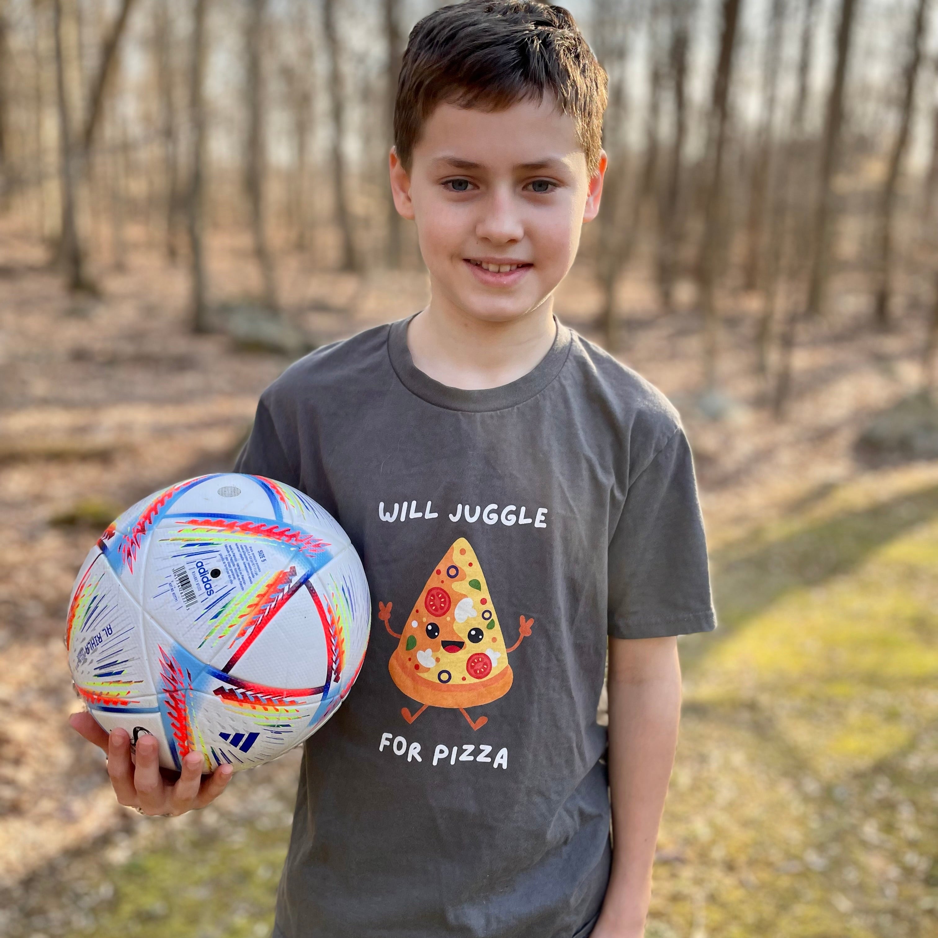 Young boy holding a soccer ball outdoors in a forested area